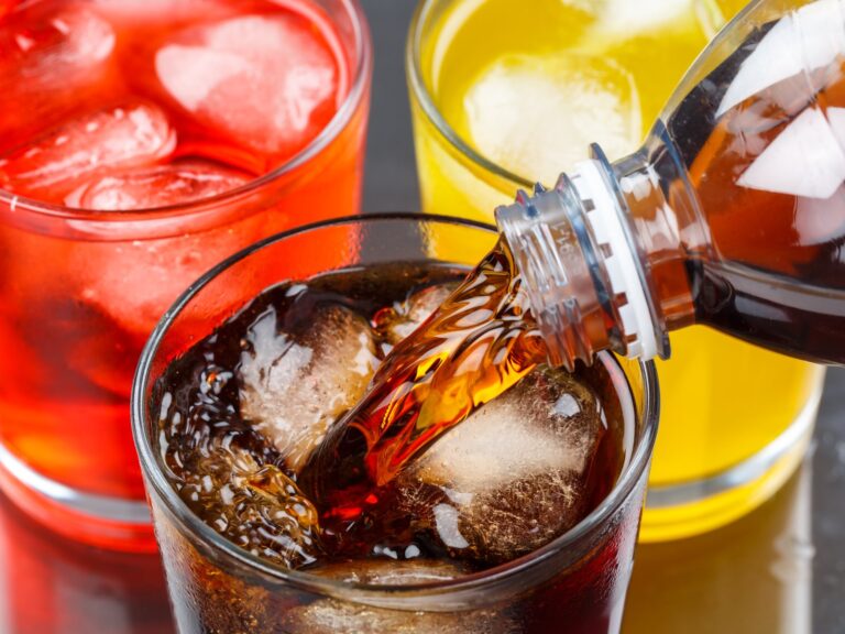 Cola wird über Eis ins Glas gegossen, daneben Limonaden in Rot und Gelb