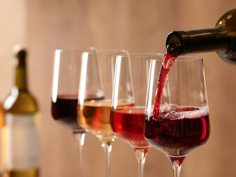 Rotwein wird in ein Glas eingeschenkt, dahinter eine Reihe gefüllter Weingläser